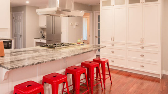 kitchen renovation with marble countertop, hood range, new kitchen cabinets, and red bar stools.